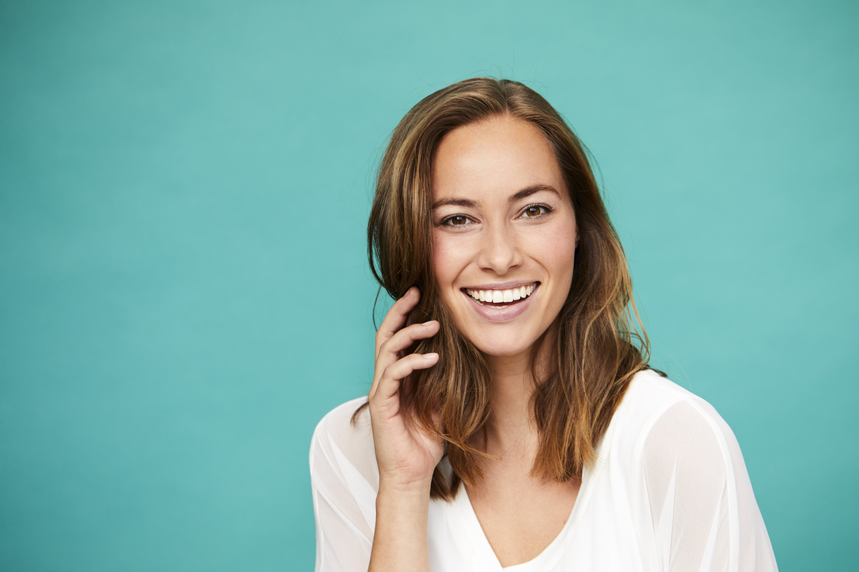 A woman with an amazing smile in front of a teal-colored background.