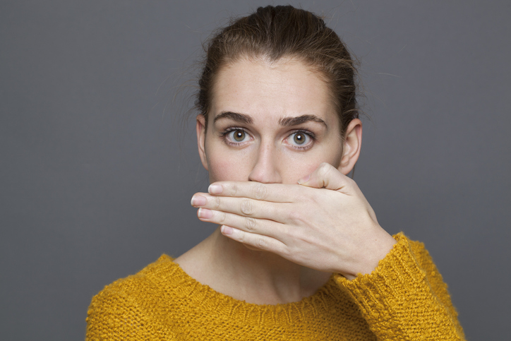 Woman in a yellow sweater covering her mouth with her hand because of bad breath.